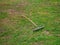 Old vintage rusty metal rake with a wooden handle on the ground with green grass