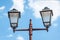 Old vintage and rusty street lamp post or lantern with two light bulbs against beautiful blue sky with white clouds background, re