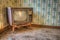 Old vintage television set in an abandoned room with faded wallpaper.