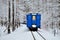 An old vintage train with beautiful blue Passenger cars rides by rail through a winter snowy forest.