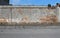 Old wall with  peeled plaster and exposed bricks. Porphyry sidewalk and asphalt road in front,