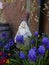 Old weathered garden gnome stands in front of a brick wall in a flowerbed