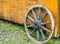 Old weathered wagon wheel with wooden spokes leaning against a yellow wooden box