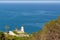 Old white lighthouse on the green hill with palms above the sea