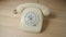 Old white rotary telephone with twisted cord on beige wooden table. Retro landline phone with rotary dialer and handset