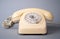 Old white rotary telephone with twisted cord on gray background. Retro landline phone with rotary dialer and handset