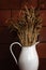 Old and white rustic pitcher with dry rye in front of brown wall