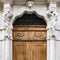 Old white stone entrance with statues and wooden portal.