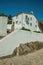 Old whitewashed wall house over rocks with stairs and plants