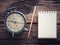 Old wind clock with notebook and pencil on wood table in vintage color scheme