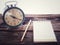 Old wind clock with notebook and pencil on wood table in vintage color scheme
