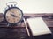 Old wind clock with notebook and pencil on wood table in vintage color scheme