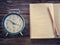 Old wind clock with notebook and pencil on wood table in vintage color scheme