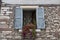 Old window with open shutters with flowers on the window sill on the stone wall. Italian Village