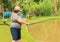 Old woman holding a fishing rod, hooking a fish on a lake.