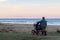 An old woman rides on a electric powered wheelchair parked on the beach at sunset time, in a lonely atmosphere. Lonely widow old
