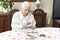 The old woman sits at a table with a newspaper.