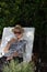 old woman sitting on a deck chair drinking mate in the garden of her house