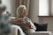 Old woman sitting on sofa holding cup looking out window