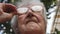 Old woman straightens her glasses and looking forward. Portrait of grandmother outdoor. Granny wearing eyeglasses