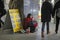 An old woman street beggar counting money sitting near currency exchange, people pass by