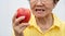 An old woman wears glasses and without teeth trying to eat red apples. Concept of Dental health problems, Elderly patients medical