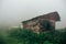 Old wooden abandoned house on green grass among dense fog, mist