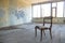 An old wooden broken chair in the middle of an empty dilapidated room. Poverty and ruin. The apartment is without repair and