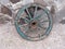An old wooden cartwheel with a broken spoke. Cracked wooden elements painted with blue paint. Leaning against a stone wall