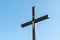 An old wooden Christian cross against a clear blue sky on a beautiful summer day. A statuette of Jesus in the center of the cross