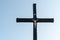 An old wooden Christian cross against a clear blue sky on a beautiful summer day. A statuette of Jesus in the center of the cross