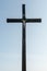 An old wooden Christian cross against a clear blue sky on a beautiful summer day. A statuette of Jesus in the center of the cross