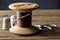 OLD WOODEN COTTON REEL WITH STRONG BROWN COTTON THREAD, A NEEDLE AND THIMBLES AND A PAIR OF SCISSORS IN THE BACKGROUND