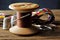 OLD WOODEN COTTON REEL WITH STRONG BROWN COTTON THREAD, A NEEDLE AND THIMBLES, A PAIR OF SCISSORS AND A COLORFUL HTREAD BRAID IN T