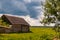 Old wooden country house amidst golden-green field and brooding dark clouds on a bright sunny day