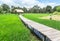 Old wooden curve walkway bridge crossing rice field to old bamboo hut