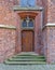 Old wooden door in brick wall with iron fittings, steps and ornamental windows