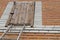 Old wooden door to the attic on rusty metal hinges, closed with a turntable lock and the top of metal ladder leaned to it