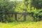 Old wooden enclosure with gate in forest in countryside. Green grasses and trees in sunny day