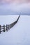 Old wooden farme fence in a winter rural landscape with dark clouds and snow