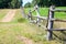 Old wooden fence with barbwire around green meadow near rural road, nobody