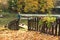 Old wooden fence, bike among the fallen autumn leaves on the shore near the water. Fisherman with a fishing rod