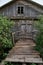 Old wooden grey hut in the village. Old time watermill among green trees in countryside. Doors of ancient wooden building