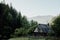 Old wooden house with a fence at the foot of the mountain with a growing forest and mountains in the background