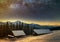 Old wooden house, hut and barn, pile of firewood in deep snow on mountain valley, spruce forest, woody hills on dark starry sky