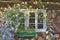 An old wooden house window, a garden full of flowers around the house