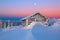 Old wooden hut. Huge snowdrifts around. Background of the high mountains. High fairtrees freezed with snowflakes.