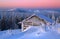 Old wooden hut. Huge snowdrifts around. Background of the high mountains. High fairtrees freezed with snowflakes.