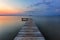 Old wooden jetty, pier reveals views of the beautiful lake, blue sky with cloud. Sunrise enlightens the horizon with orange warm