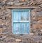 Old wooden light blue window in a wall of rocks